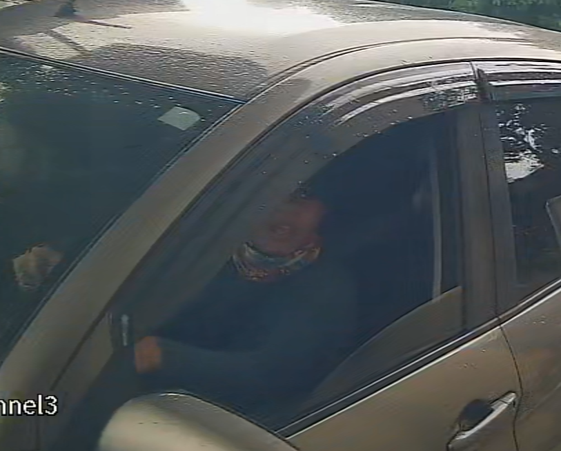 The driver at the window of the vehicle, wearing a patterned face covering, face not identifiable